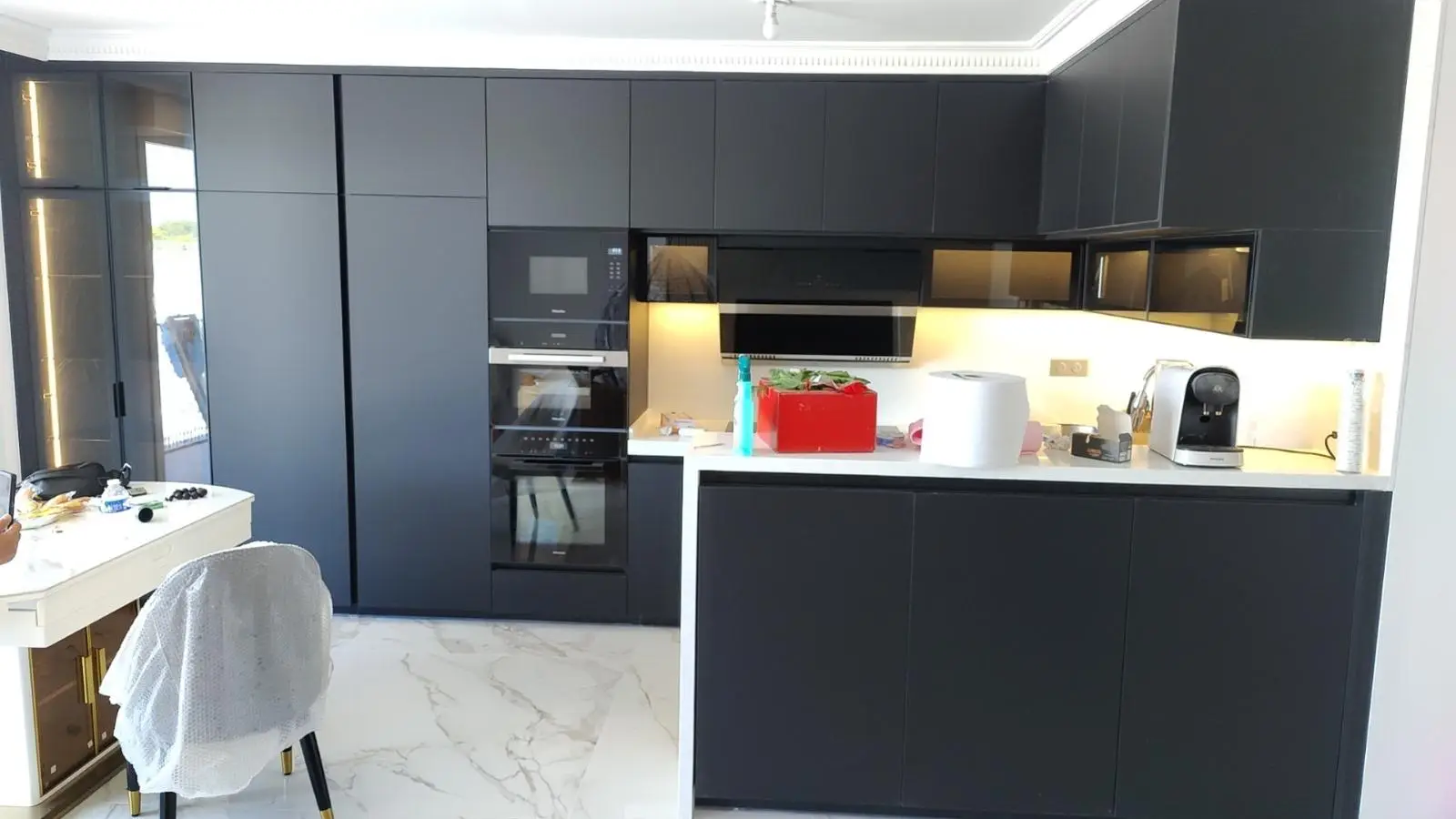 Dark handle-free kitchen with integrated ovens and a marble-topped island
