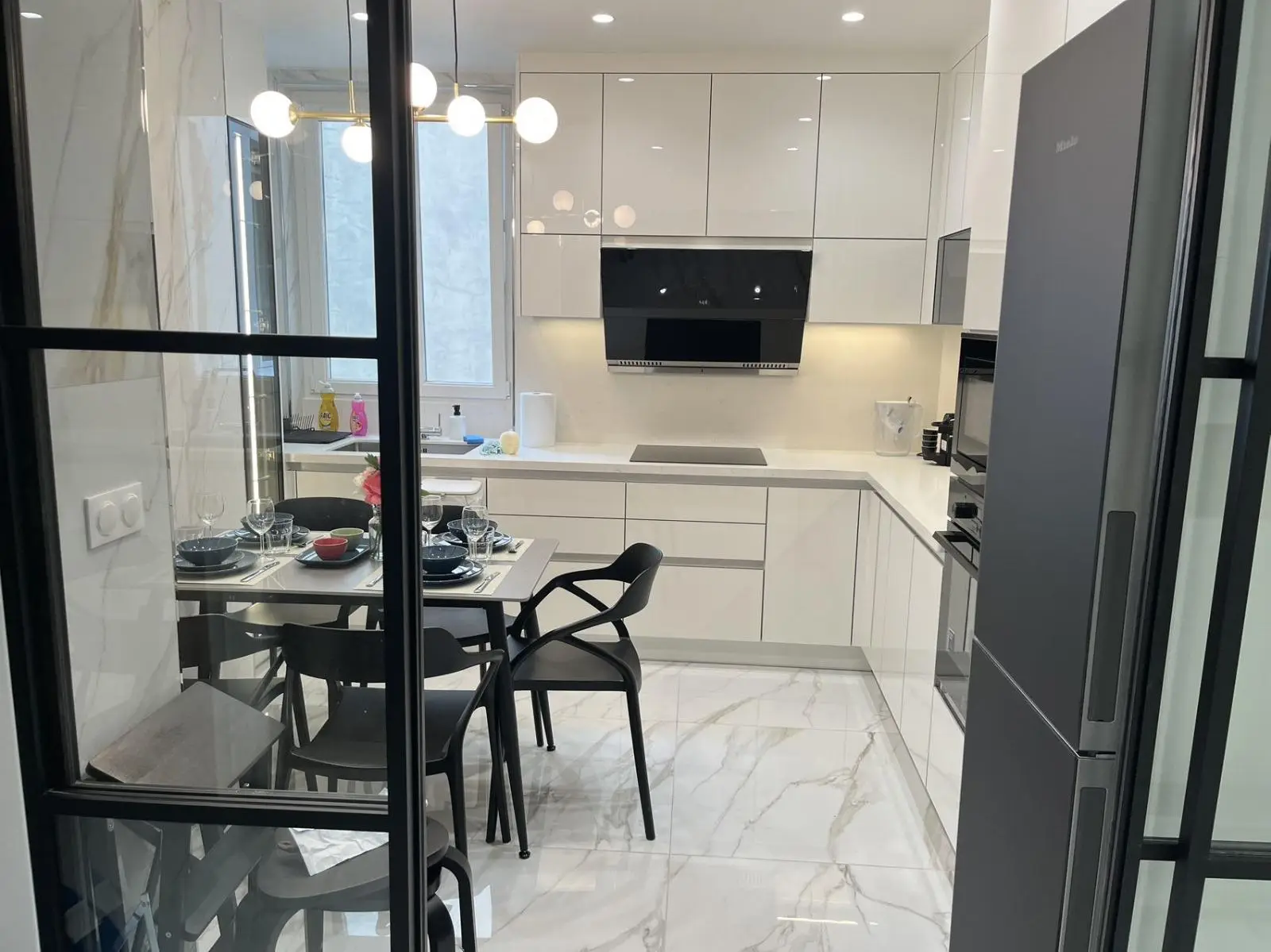 Handle-free kitchen with marble surfaces seen through Crittall doors