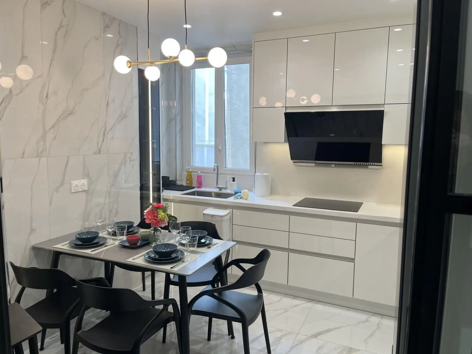 Handle-free gloss kitchen with marble splashback, integrated appliances and a dining table beneath cluster pendants