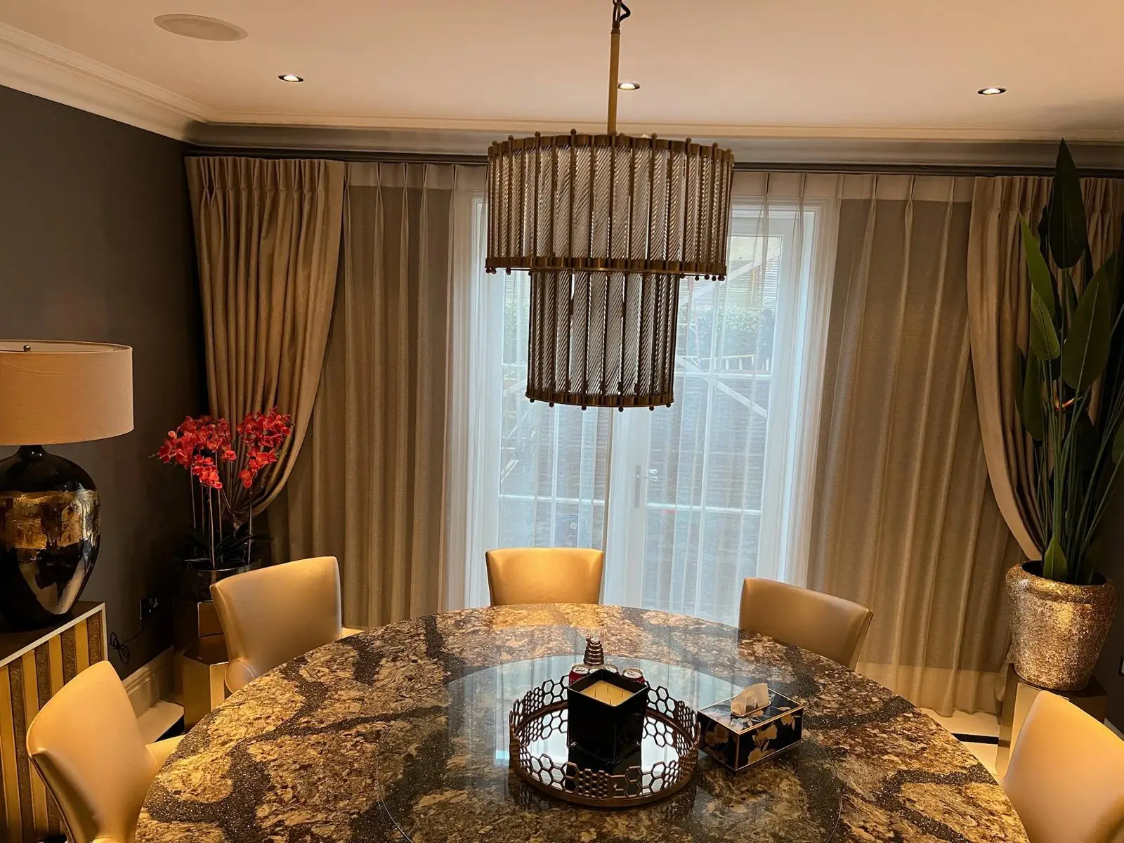Formal dining room with a stone-topped table, upholstered chairs, full-height curtains and a linear pendant