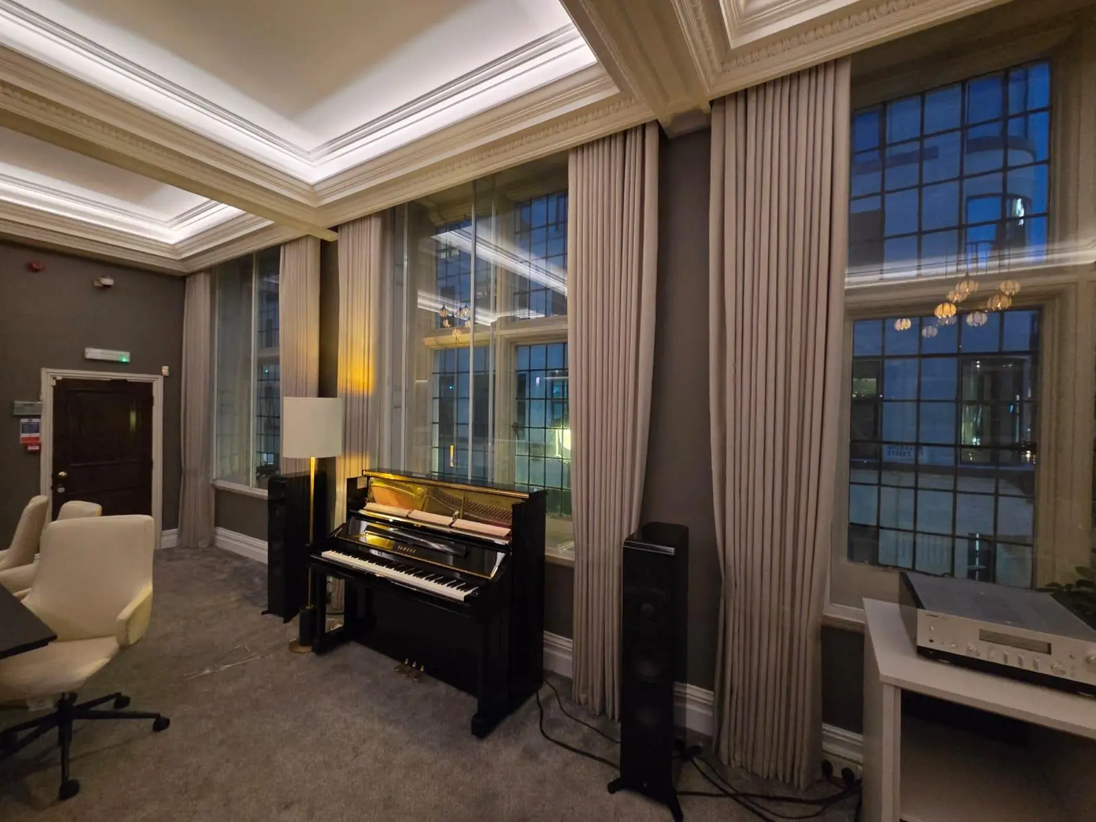 Yamaha Music boardroom at dusk — curved sofa, stone-topped tables and armchairs beneath a coffered ceiling, with full-height curtains to the original windows